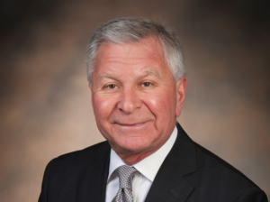 Portrait of Bob Grubic wearing a dark suit coat, white shirt, and gray tie