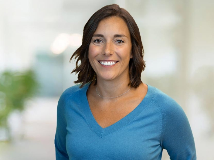 Photo of Erin Threet wearing a light blue, v-neck sweater and standing in front of a blurred office background