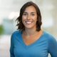 Photo of Erin Threet wearing a light blue, v-neck sweater and standing in front of a blurred office background