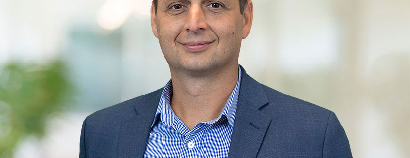 Justin Mendinsky wearing a smoky blue jacket and brighter blue, patterned and collared shirt.