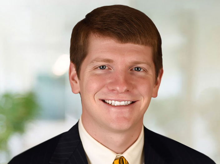 Justin Peaslee wearing a black suit coat, white shirt, and yellow tie.