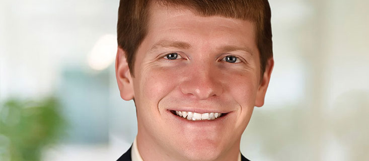 Justin Peaslee wearing a black suit coat, white shirt, and yellow tie.