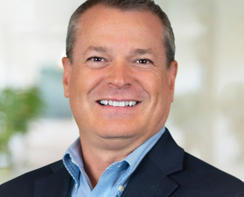 Thomas Farmar wearing a light blue button-down shirt and dark suit coat.