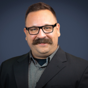 James Meisenbach wearing a black jacket and black and white printed shirt.