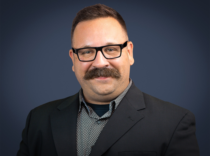 James Meisenbach wearing a black jacket and black and white printed shirt.