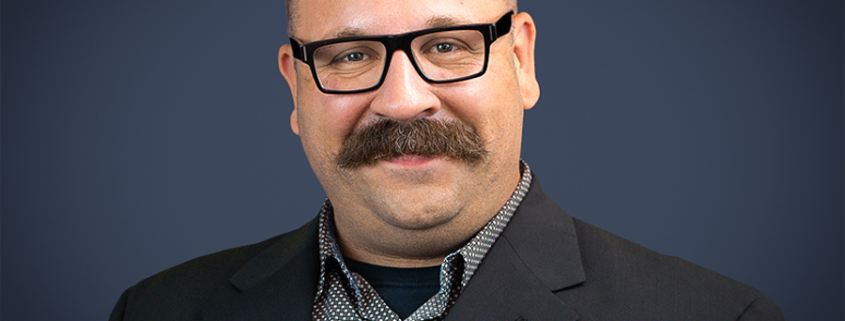 James Meisenbach wearing a black jacket and black and white printed shirt.