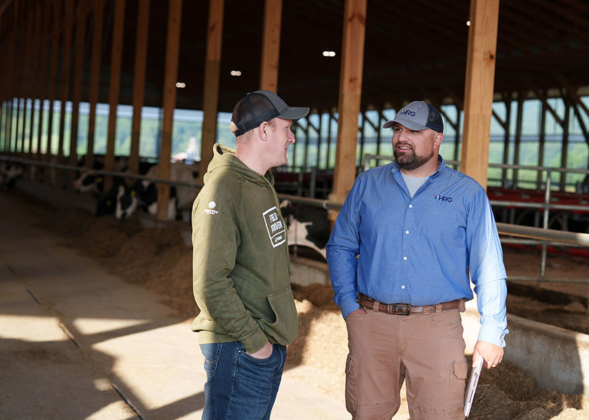 Nick Hepfl listens to a farmer talk about his needs. The two are standing in a cattle barn.